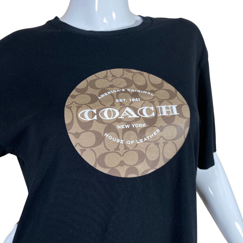 Load image into Gallery viewer, Coach Black Tee with Monogram is a black short-sleeve T-shirt featuring a Coach logo design on the front - closeup view
