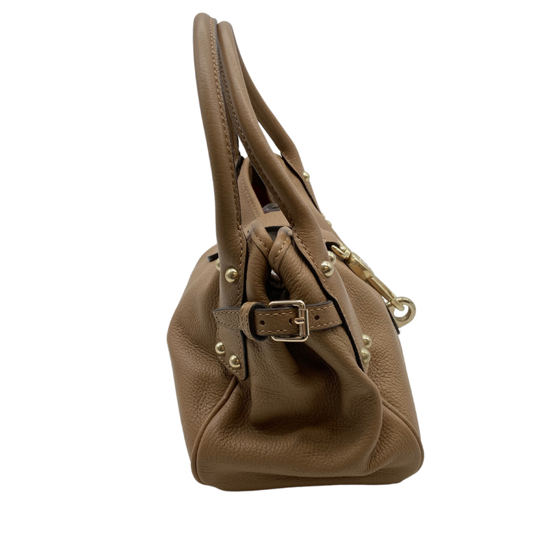 Load image into Gallery viewer, Pre-loved Dooney Bourke Light Brown Handbag is a stylish, medium-sized beige leather handbag with a pebbled texture. It features gold-tone hardware, including a decorative clasp on the front with an engraved logo and studded details on the handle attachments - side view
