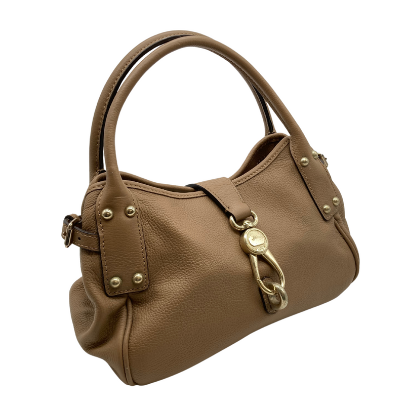 Load image into Gallery viewer, pre-loved Dooney Bourke Light Brown Handbag is a stylish, medium-sized beige leather handbag with a pebbled texture. It features gold-tone hardware, including a decorative clasp on the front with an engraved logo and studded details on the handle attachments - front view
