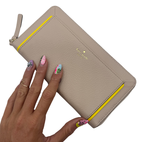 Beige wallet with yellow zipper held by a hand on a white background