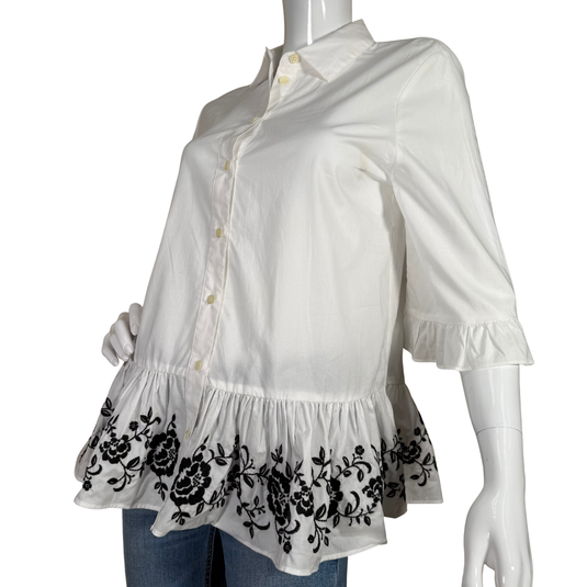 White blouse with black floral embroidery on a mannequin against a white background