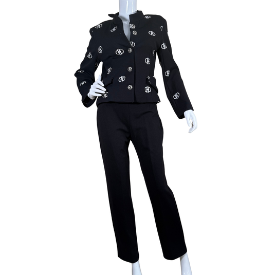 Nouritano Elegant Black Suit Set With White Embroideryt blends classic tailoring with playful branding, featuring a cropped jacket adorned with silver-tone logo embellishments throughout.